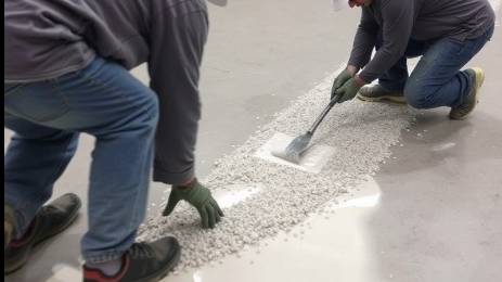 Crew double-broadcasting quartz aggregate onto wet epoxy in a construction scene.