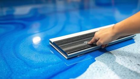 Macro view of a squeegee applying clear topcoat on blue epoxy garage floor.